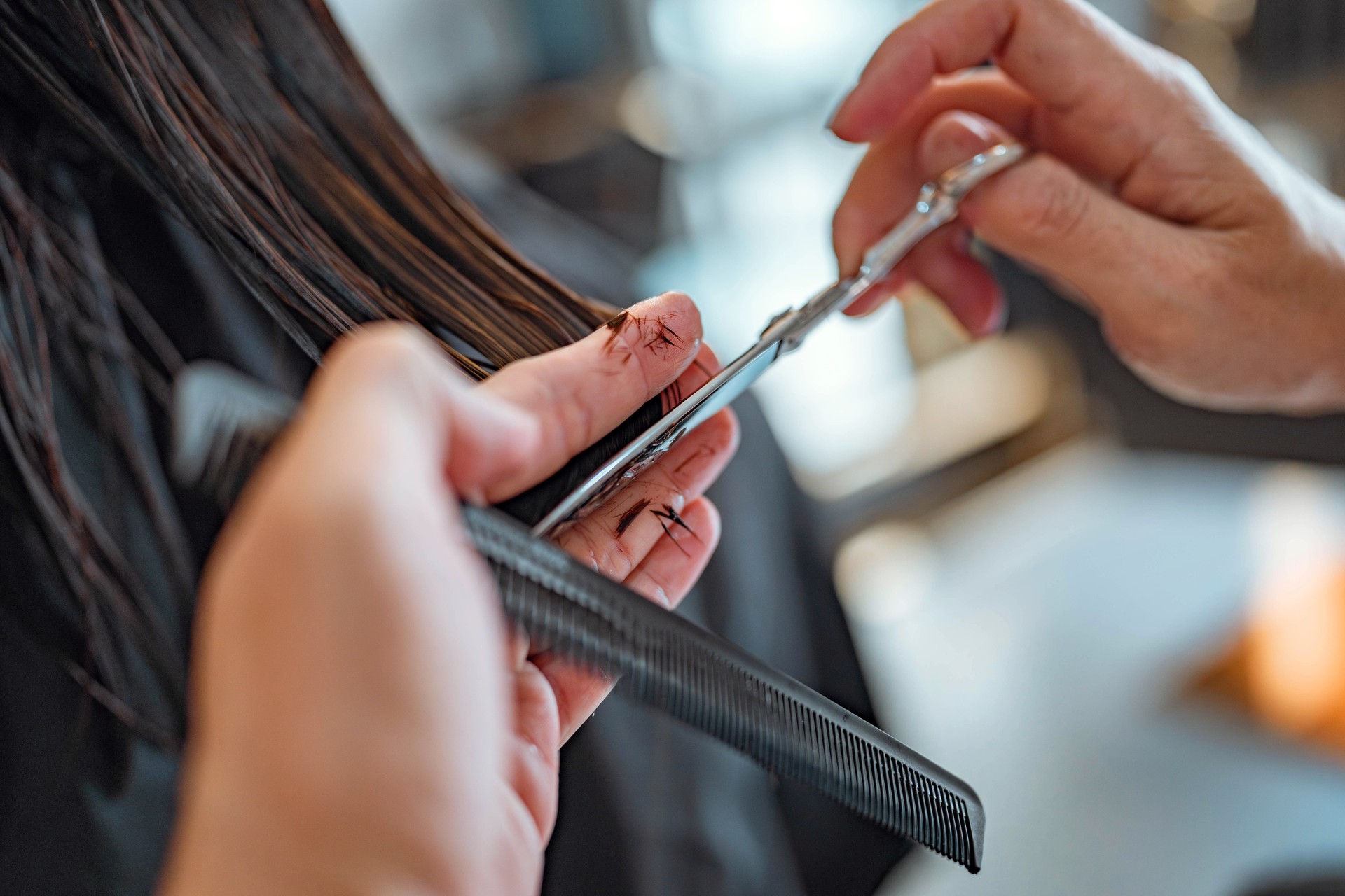 Closeup - Hands of Hairdresser trimming black hair with scissors at hair salon